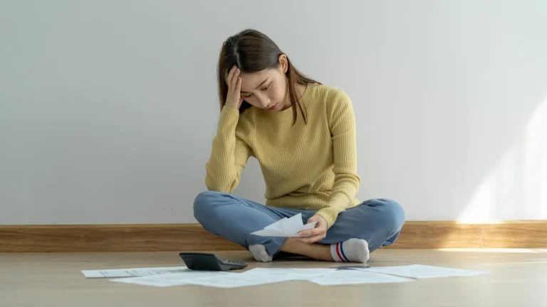 "A woman sits thoughtfully on the floor surrounded by receipts, symbolizing the weight of rising expenses and the struggle to keep up with lifestyle inflation.”