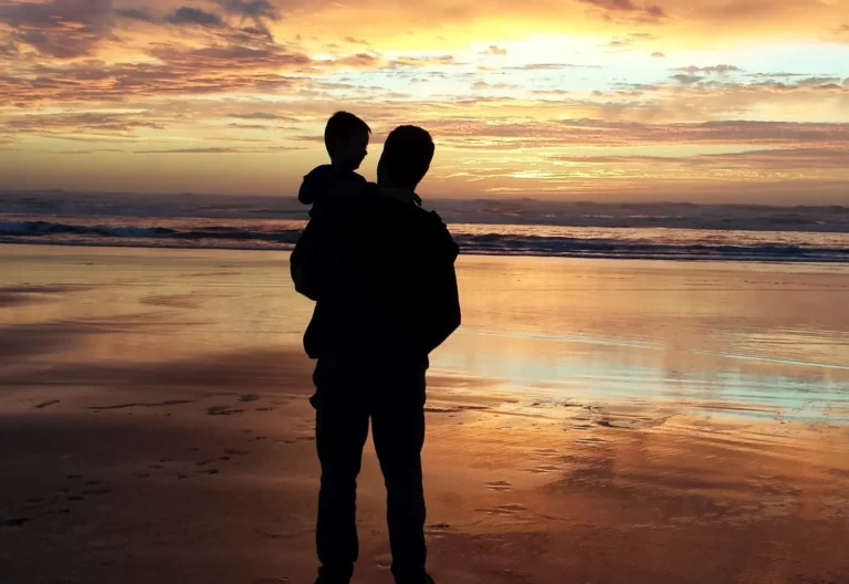 Father and child watching sunset together on a peaceful beach evening.