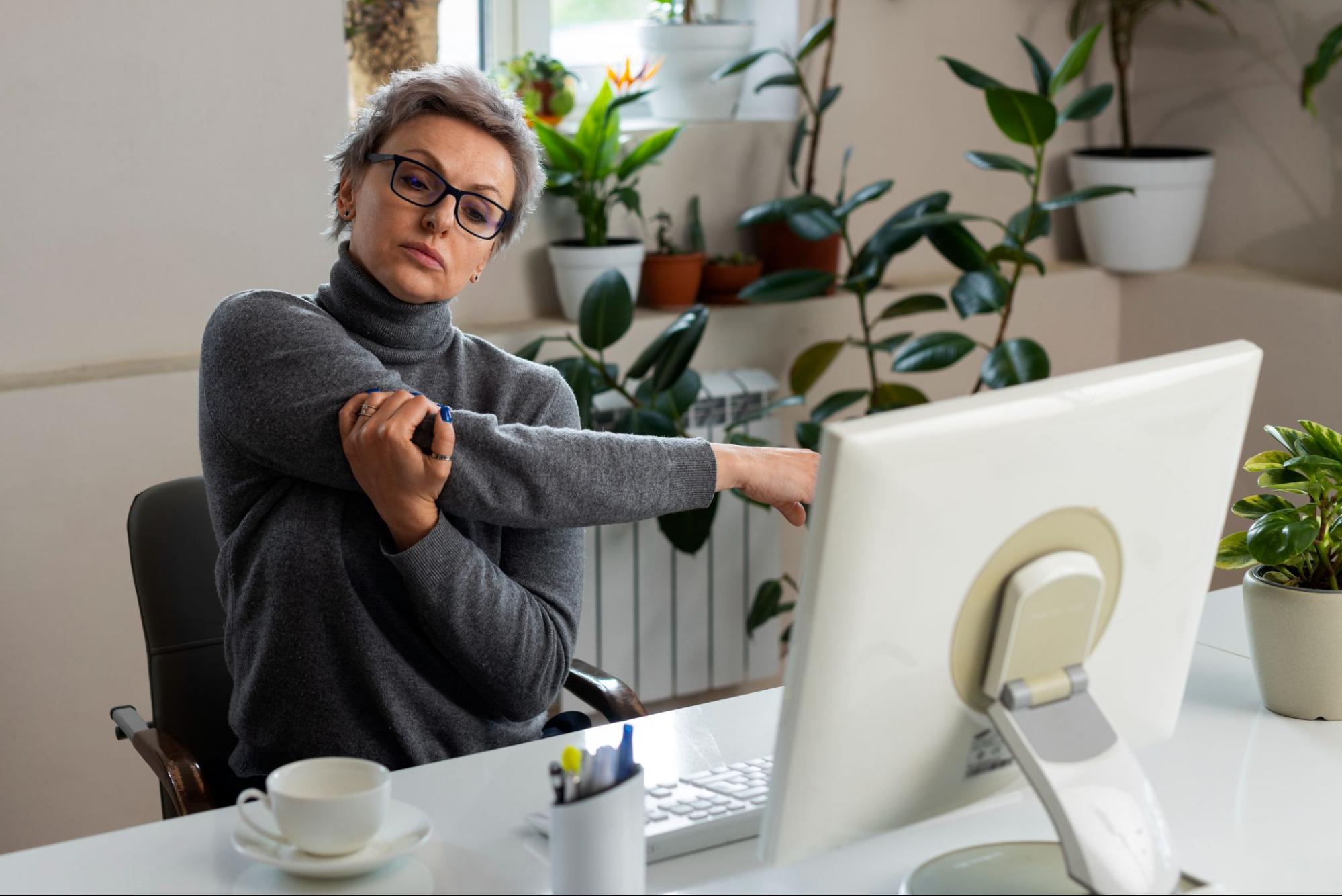 Person stretching while seated at a modern work desk in casual clothes.