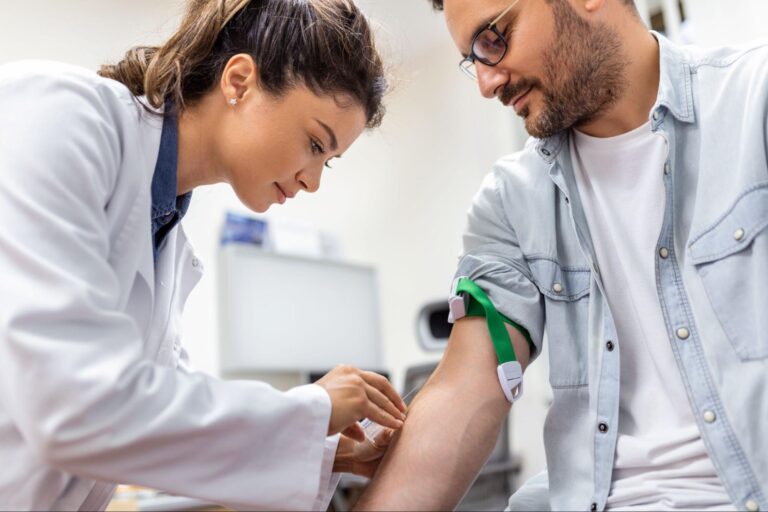 A healthcare professional gently inserts an IV catheter into a patient’s arm, with a clear fluid drip bag suspended above