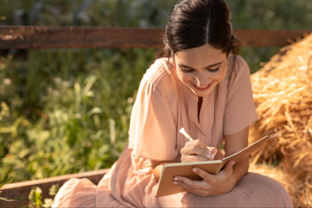 A person sitting with a journal, writing and with a peaceful smile.