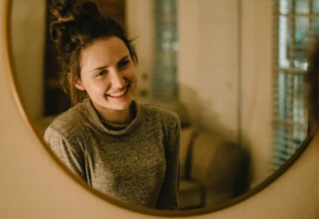 Smiling woman looks at herself in mirror, embracing personal fresh start