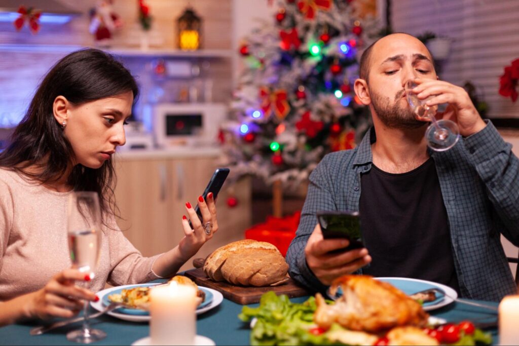 Modern-day relationship disconnect—partners distracted by work emails and messages during dinner, highlighting emotional distance.