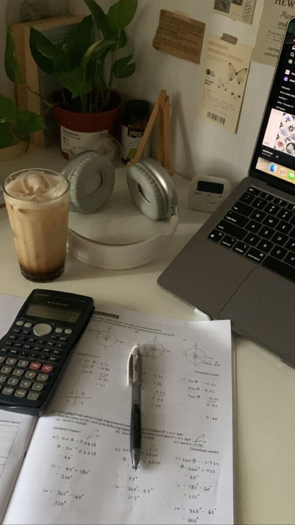 A cozy, top-down shot of a desk setup, suggesting a study session. On the left is a tall glass of iced coffee.