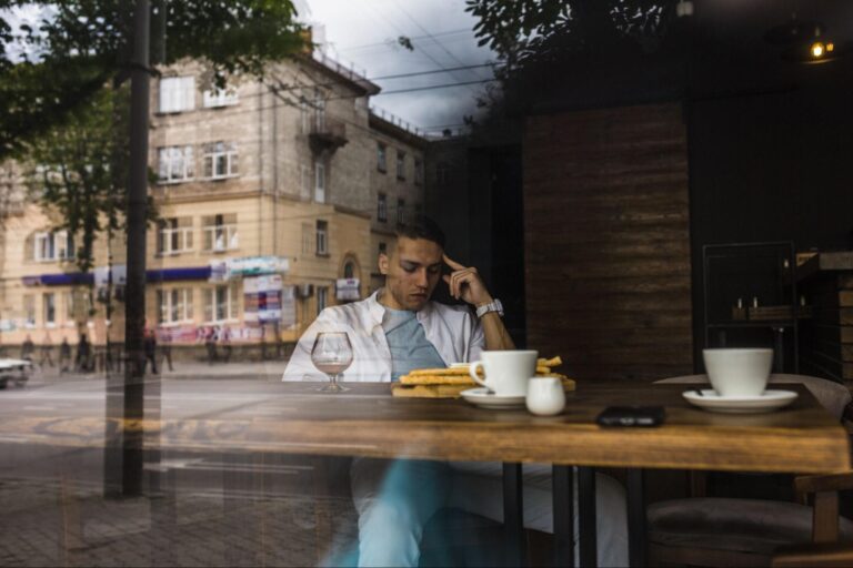 A man sitting inside a coffee shop deep into his thoughts, his face conflicted, symbolizing the internal struggle between leaving and staying in a relationship.