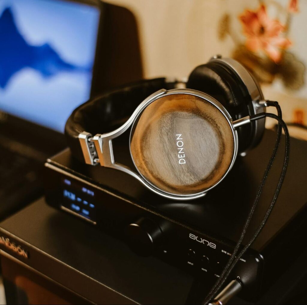 A close-up, low-angle shot of a pair of high-end Denon headphones resting on top of a black audio amplifier.