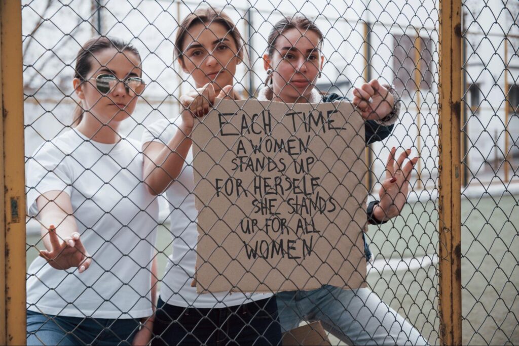 A group of diverse women holding a placard with a feminist slogan, highlighting online feminist divide.