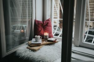 An open book sits on a wooden board next to a lit candle and a pair of glasses.
