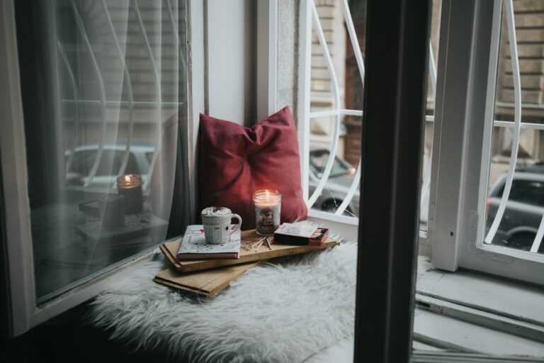 An open book sits on a wooden board next to a lit candle and a pair of glasses.