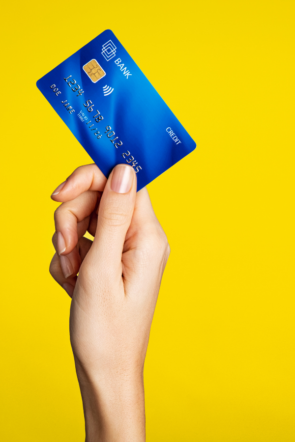 Hand holding a blue credit card against a bright yellow background.