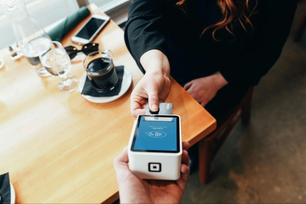 A customer inserting a chip credit card into a handheld Square terminal at a restaurant table.